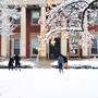 Students have a snowball fight in front of a large brick building with columns.