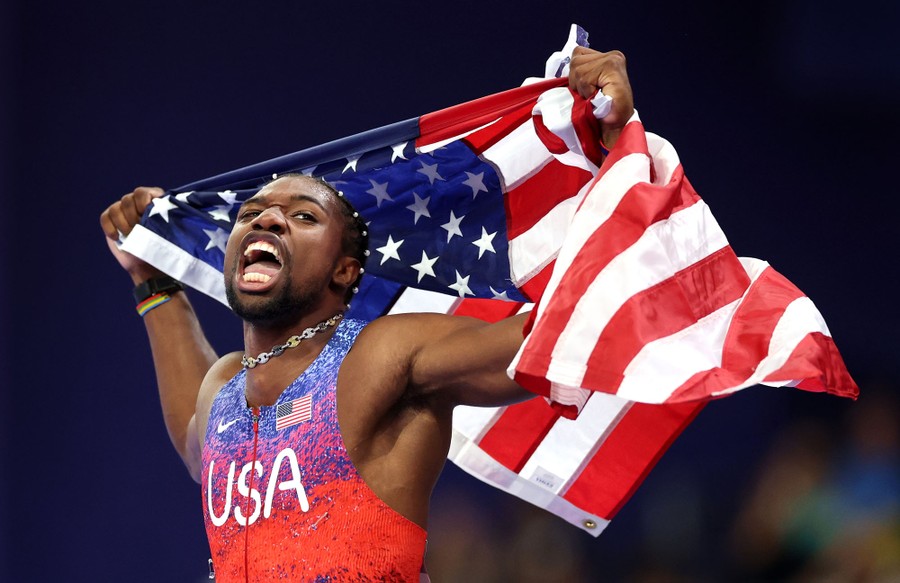 A runner with Team USA holds up an american flag after winning a race in the Olympics.
