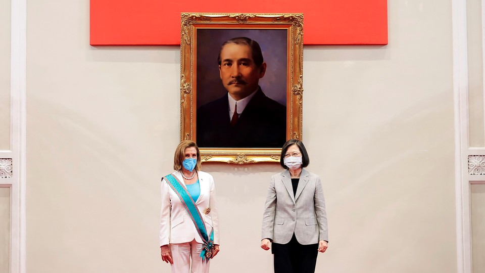 Nancy Pelosi, wearing a white pantsuit with a turquoise sash, standing with Taiwan’s president in front of a painting of Sun Yat-sen