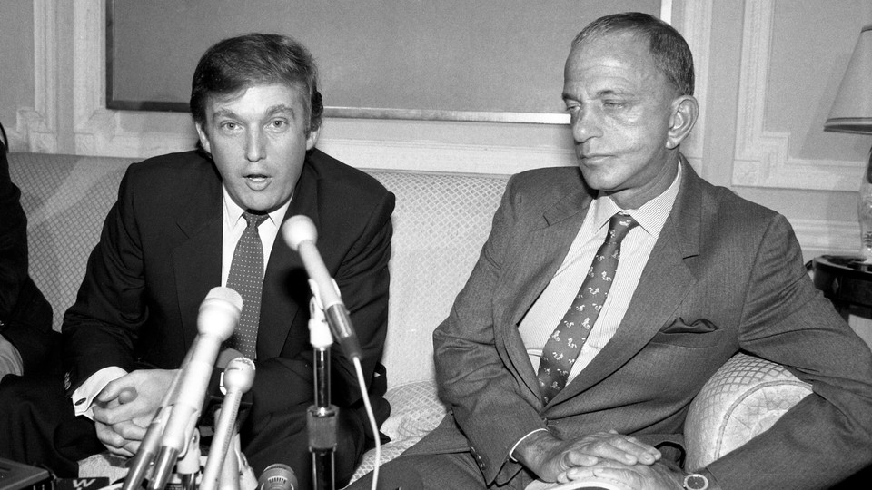 A black and white photo of Donald Trump sitting in front of microphones next to Roy Cohn.