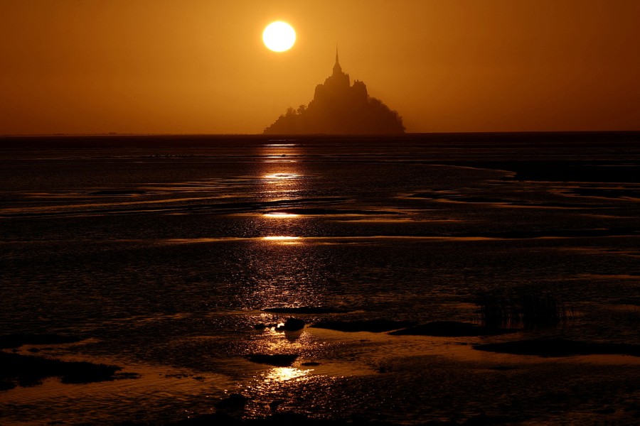 Mont Saint-Michel, seen at sunset—a historic structure built on a small rocky island that stands above a broad tidal flat.