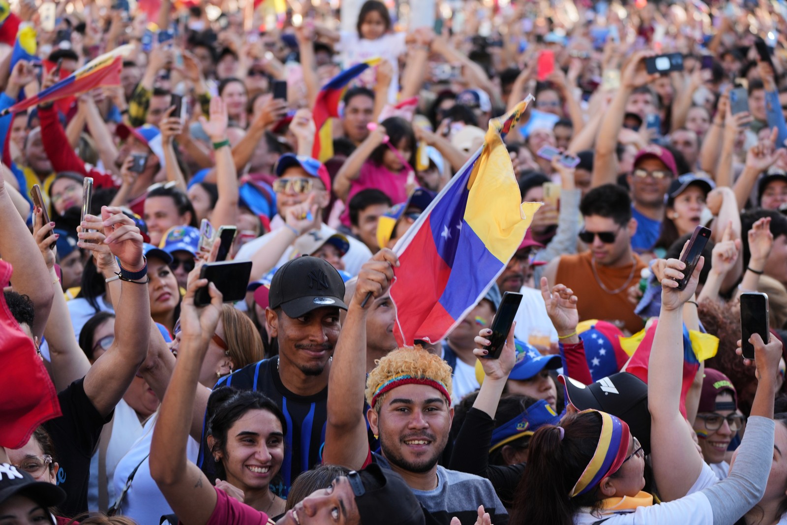 A tighter view of a crowd celebrating in a public square, one holds a Venezuelan flag.