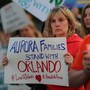 A woman at a candlelight vigil holds a sign reading "Aurora families stand with Orlando."