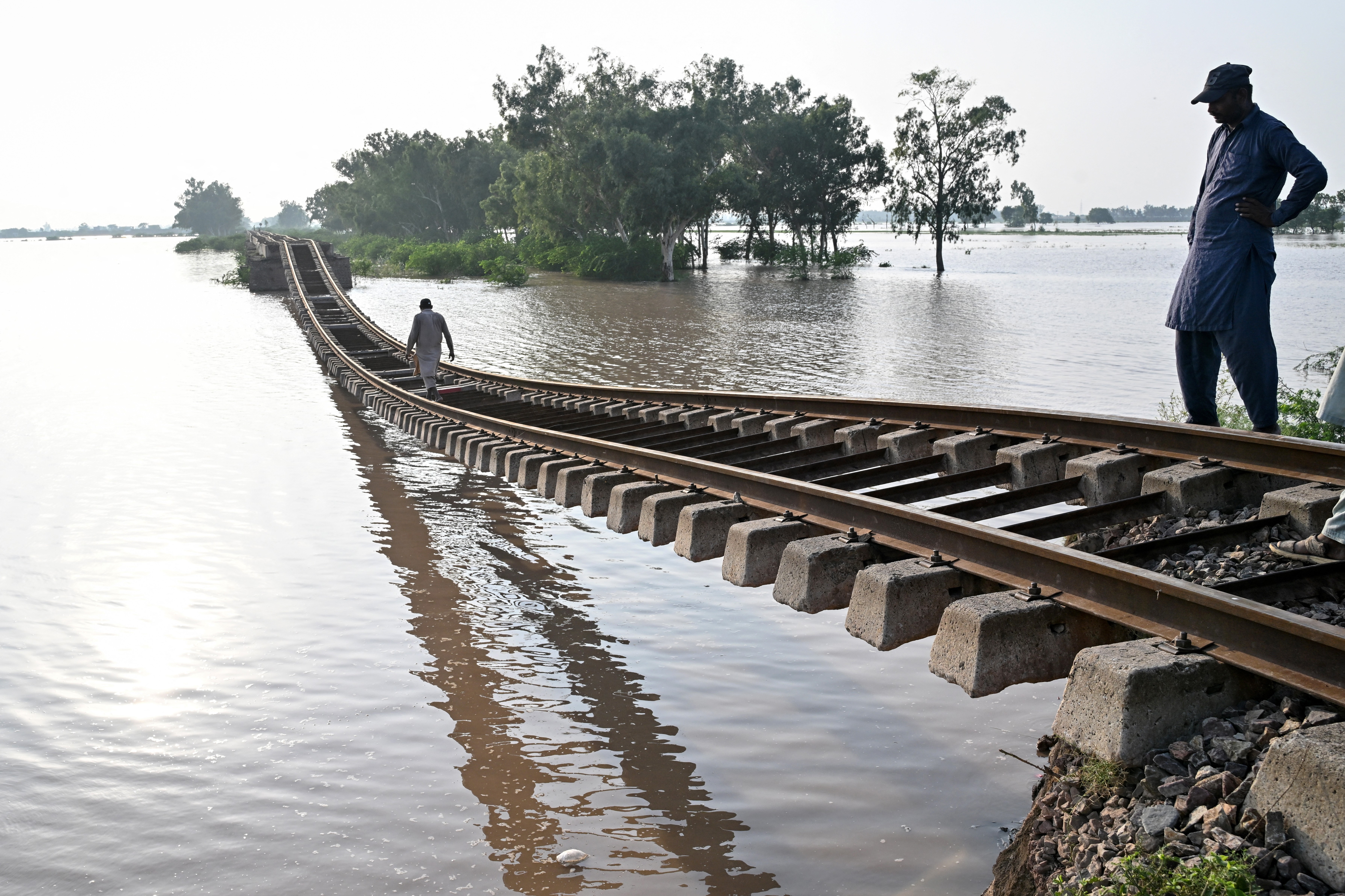 People walk across a washed-out railroad track that is hanging unsupported above a flooded area.