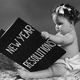 Circa 1955: A baby wearing diapers sits and holds a large book of New Year Resolutions.