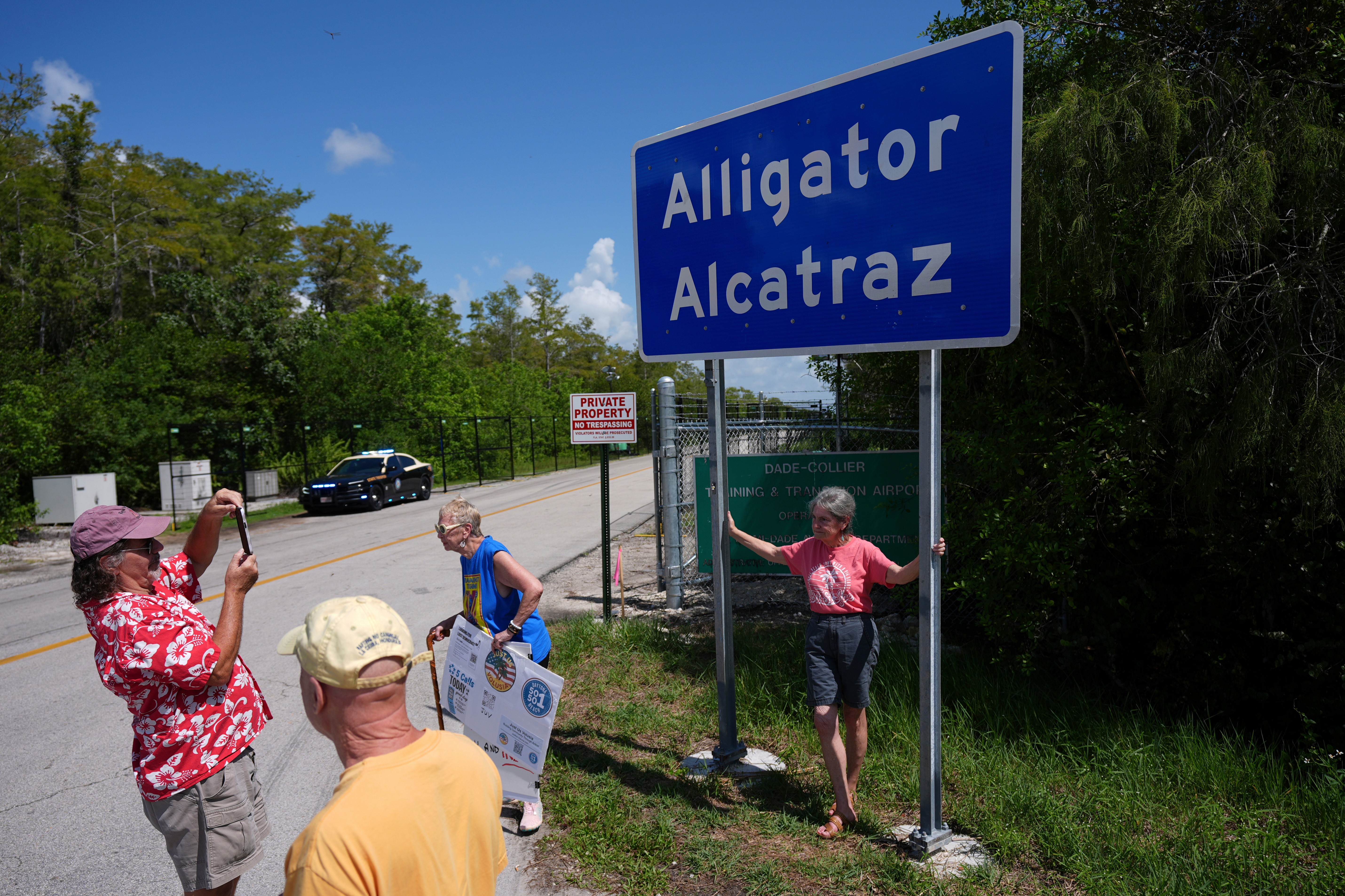 People take pictures in front of a sign reading 'Alligator Alcatraz,' alongside a road.