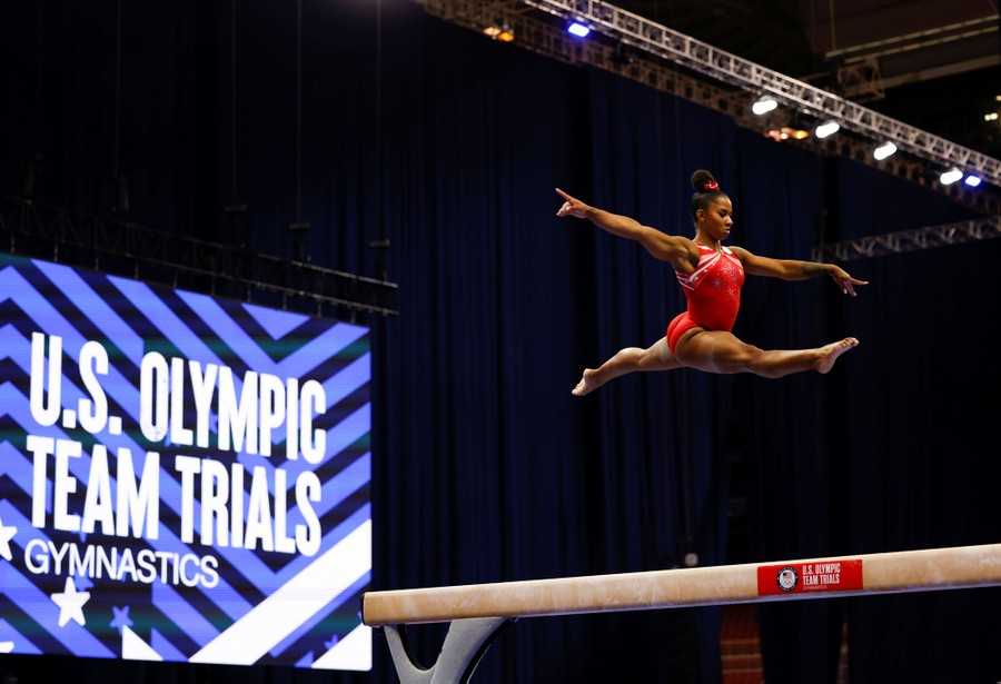 A gymnast leaps high above a balance beam.