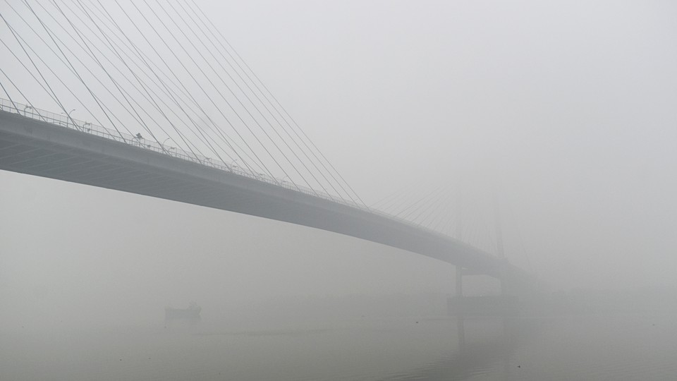 A bridge stretches over a wide river in India in thick fog.