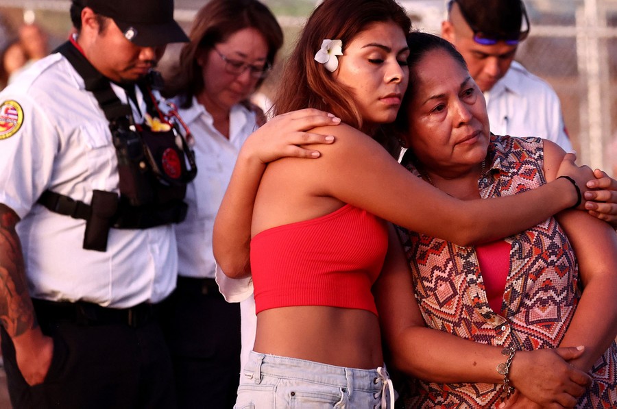 Several people stand together near a memorial, with heads bowed, or embracing.