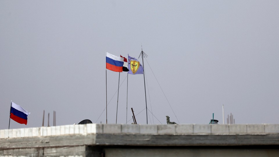 Russian, Syrian and Manbij military council flags flutter atop a rooftop in Manbjj.
