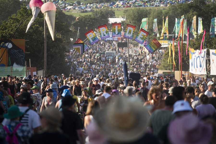 Hundreds of festivalgoers walk beneath a sign that reads "Pride."