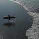 A surfer walks on the beach.
