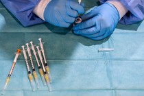 gloved hands load a vaccine into a syringe, next to an array of other vaccine syringes