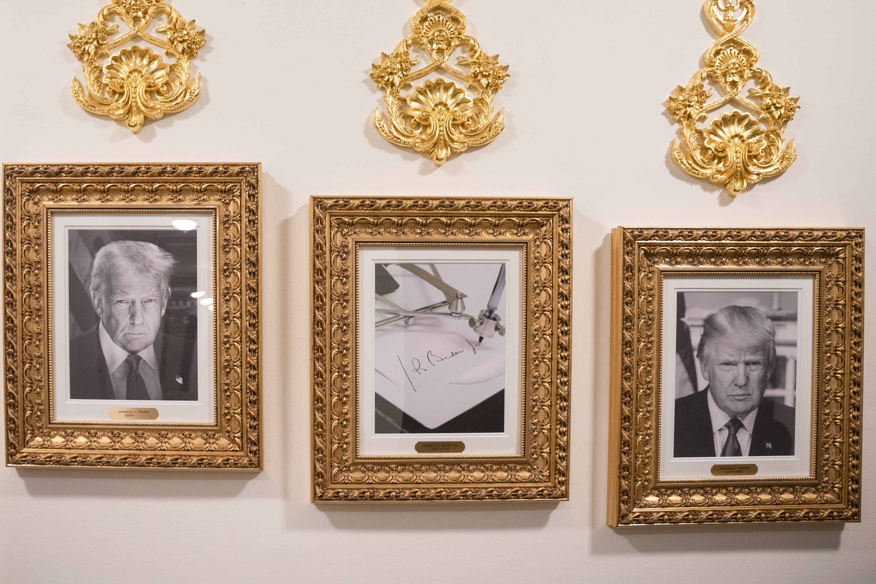 Two black and white photos of Donald Trump and in the middle is Biden's signature, all in gold frames