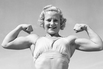 A black and white photo of a young blonde woman in a sports bra showing off large biceps