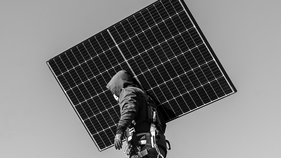 A man in a hoodie holding a solar panel in front of a gray background
