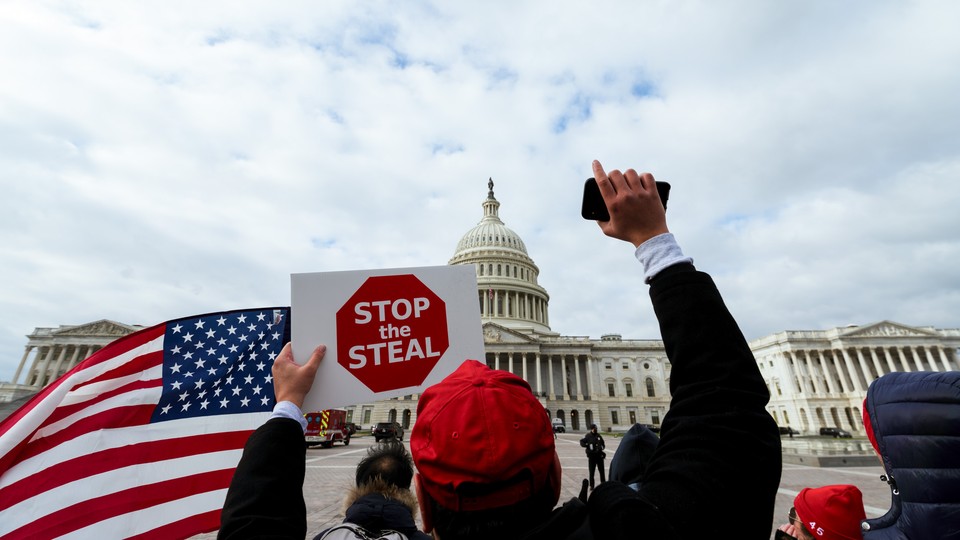 A photo of a man holding a "Stop the Steal" sign in front of the Capitol.