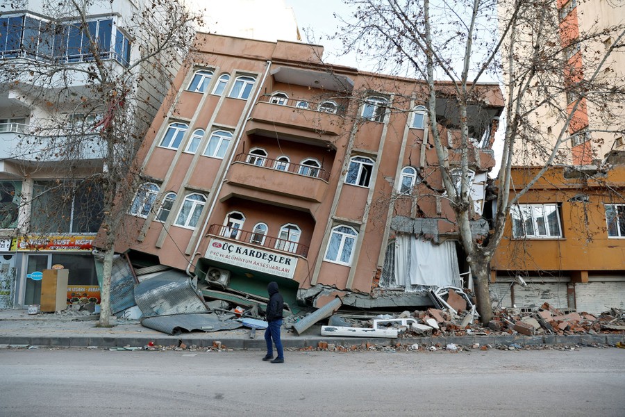 A man walks past a partially collapsed building.