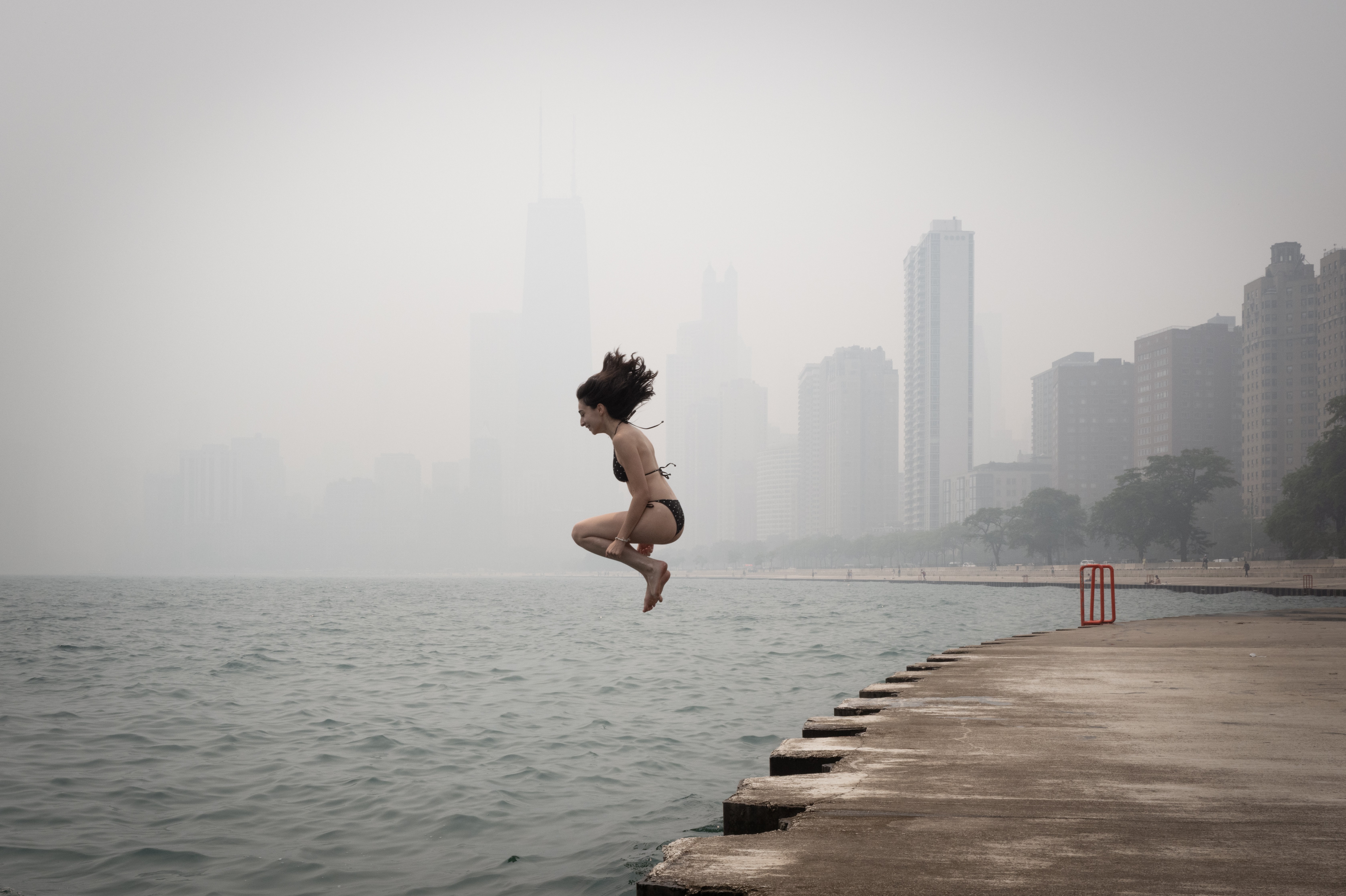 A person jumps into Lake Michigan, with Chicago buildings in the background obscured by a smoke-filled sky.
