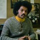 A color photograph of Jesse Jackson in his office wearing a yellow turtleneck