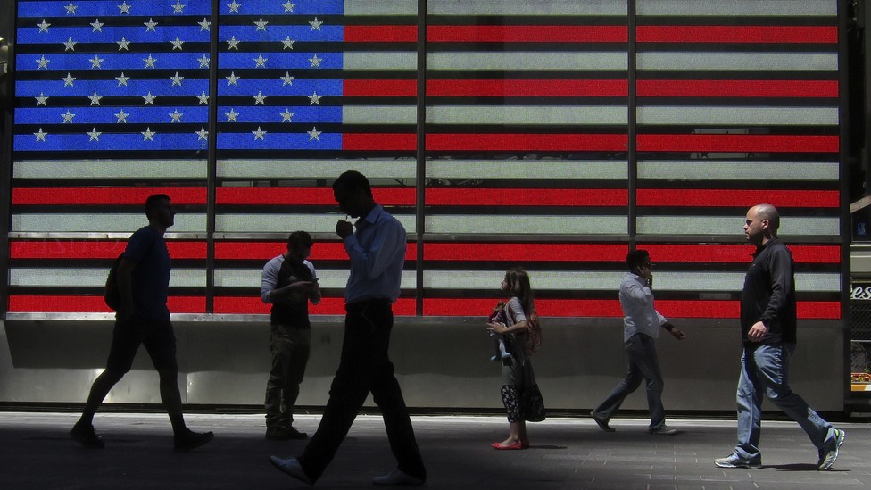Pedestrians walk past an American flag in part of Times Square in New York City.