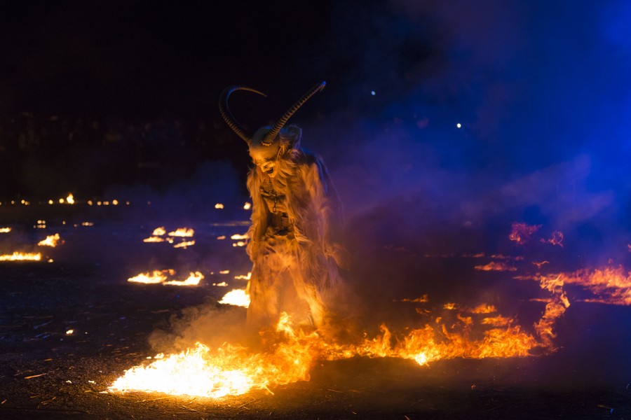 A performer dressed as a Krampus character walks through small flames.