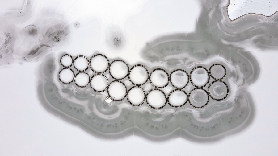 An aerial view of circular pens in a fish farm in a frozen lake.
