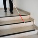 A man walks down a flight of stairs with the help of a white cane.