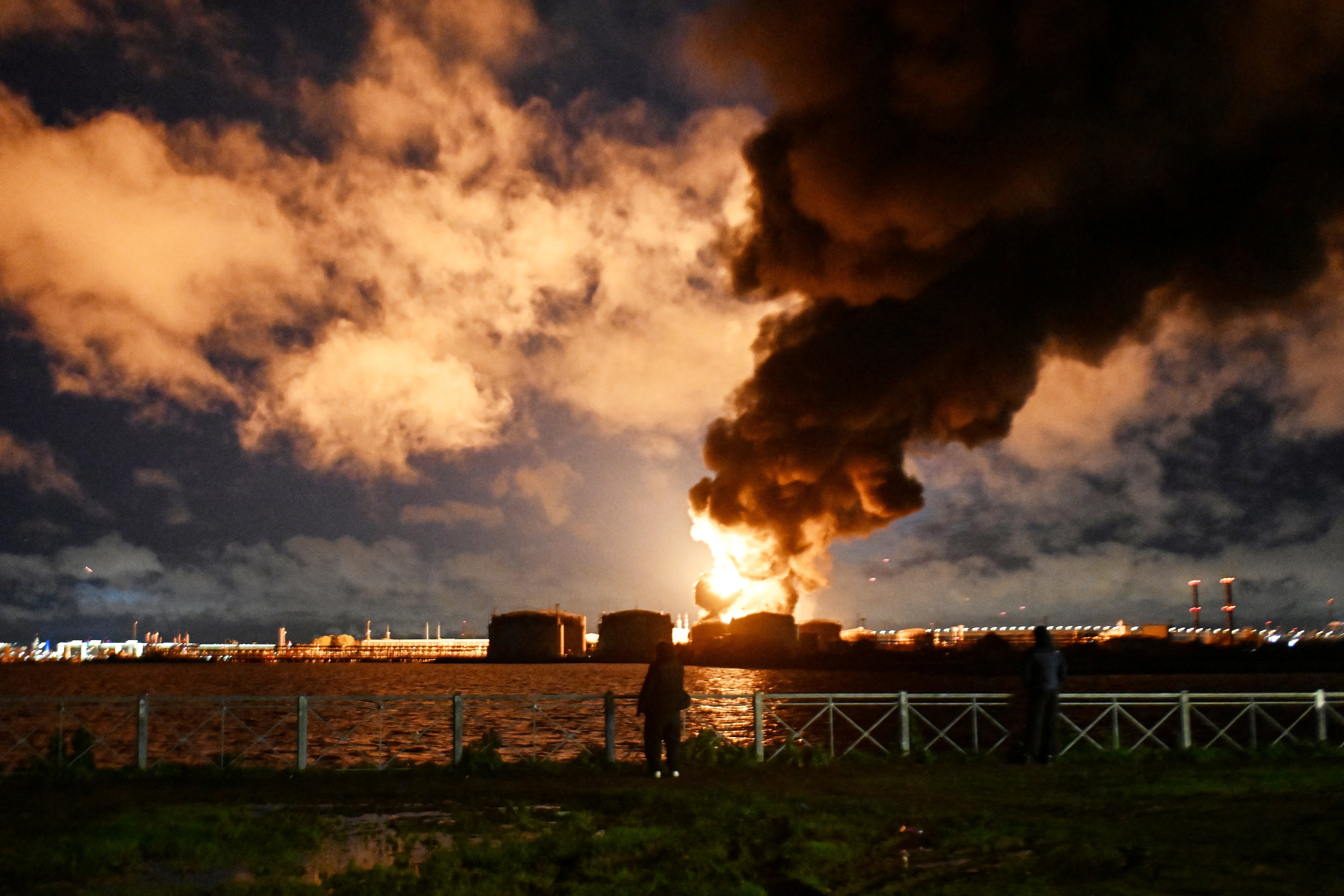 People watch a burning oil terminal.