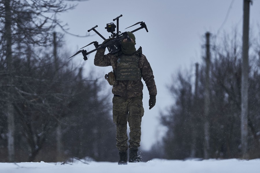 A soldier carries a drone on their shoulder while walking on a snow-covered road.