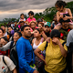 Foto de una fila abarrotada de personas con mochilas, varias de ellas con un niño sobre sus hombros, una mujer con la mano en la frente