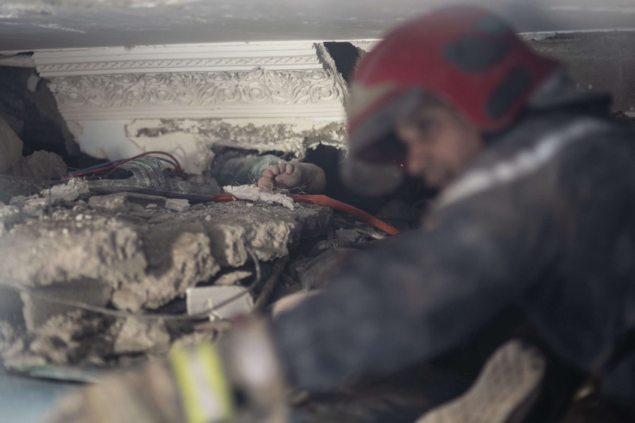 The foot of a man trapped under rubble can be seen, as a rescuer works nearby.