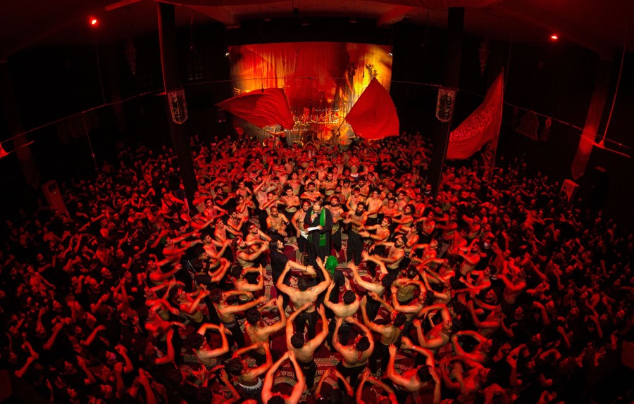 A large group of men stand gathered around a man in the center of a room.