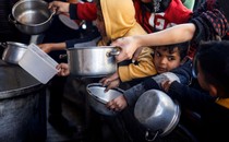 Children stand at the front of a crowd that pushes forward, holding out bowls and pots to receive food.