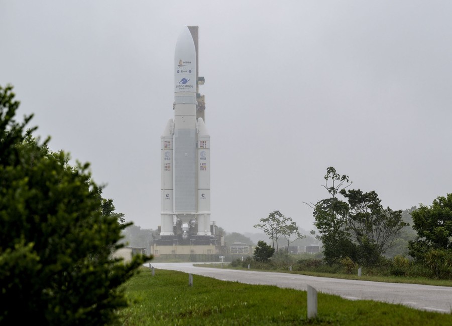 A rocketship is seen on a stand among green trees and fog.