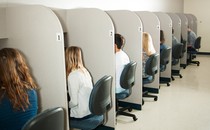 Picture showing nine teens sitting down in a line of nine cubicle desks.