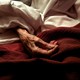 red blanket on hospital bed with an elderly hand on top