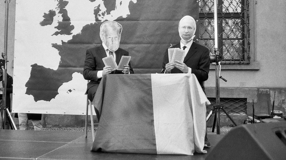 Two men play cards on a stage in front of a map of Europe, their faces obscured by cut-outs of Trump and Putin.