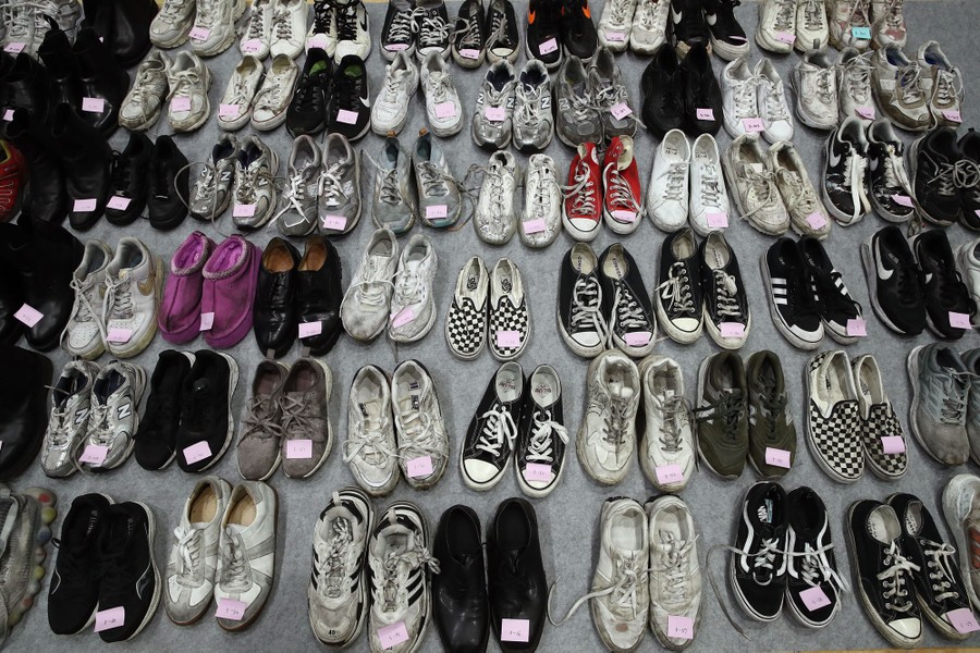 Dozens of pairs of shoes are arranged on a floor, with each left shoe bearing a sticky note with a number.