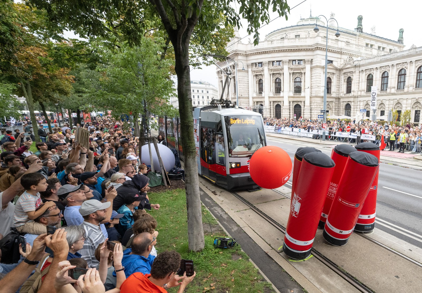 A crowd of people gather together to watch a tram driver drive their vehicle into a large inflated ball, using it to knock down 