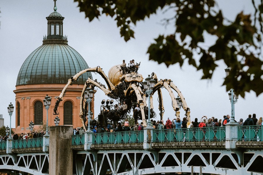 Several puppeteers ride on a giant mechanical spider puppet as it moves across a bridge.