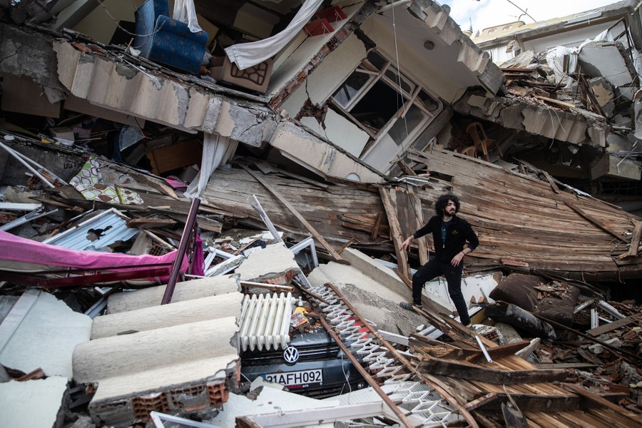 A man stands on a pile of debris beside a collapsed building.