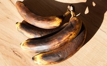 Four very brown bananas laid on their side on a wood surface