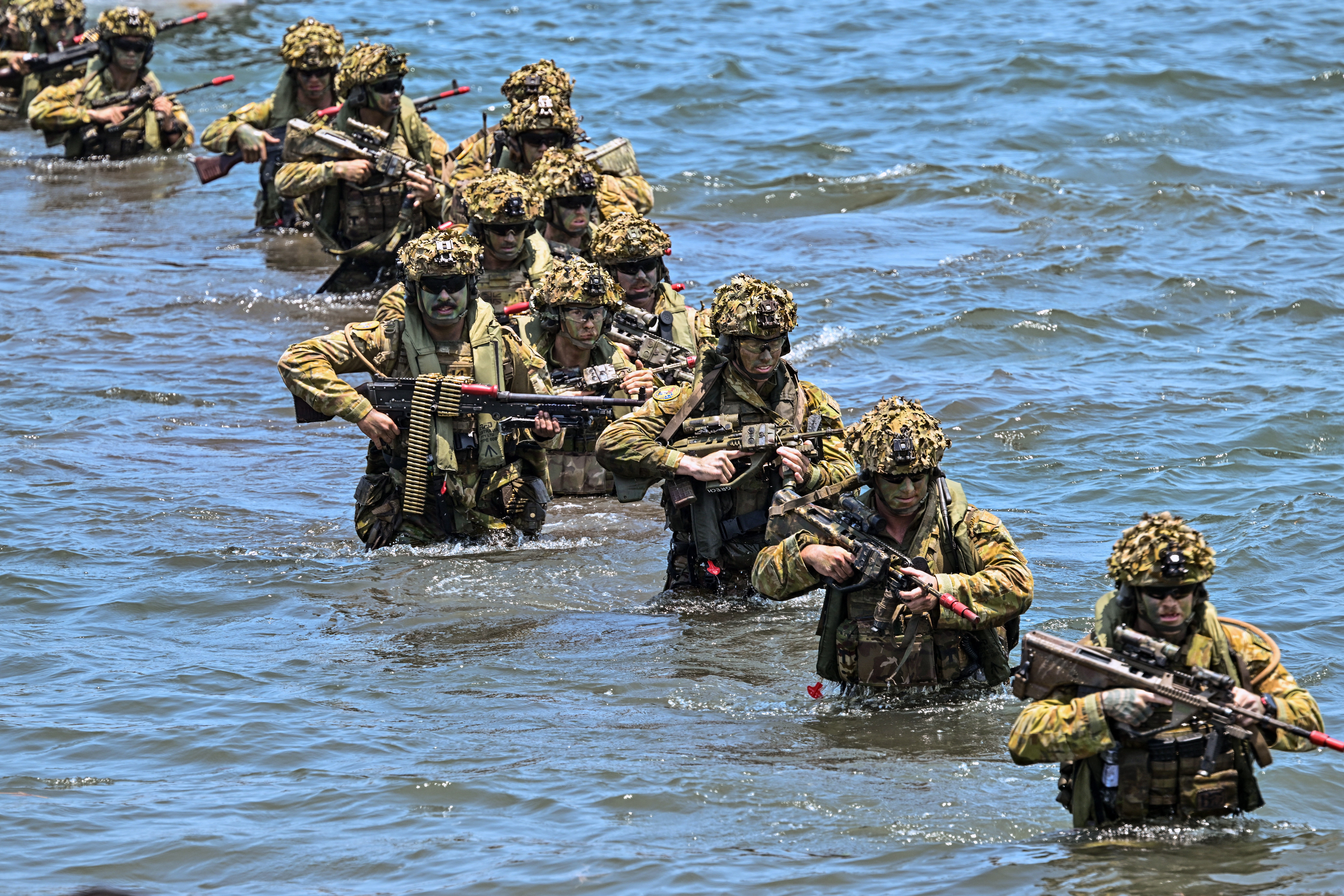 Soldiers carry long guns and heavy gear as they wade through waist-deep water.