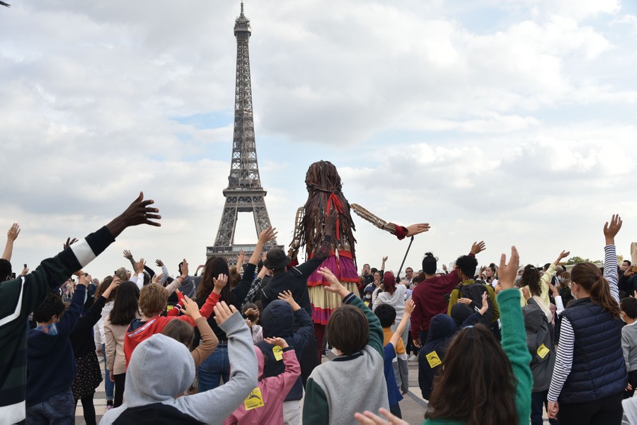 People gather around a giant puppet and wave together in front of the Eiffel Tower.