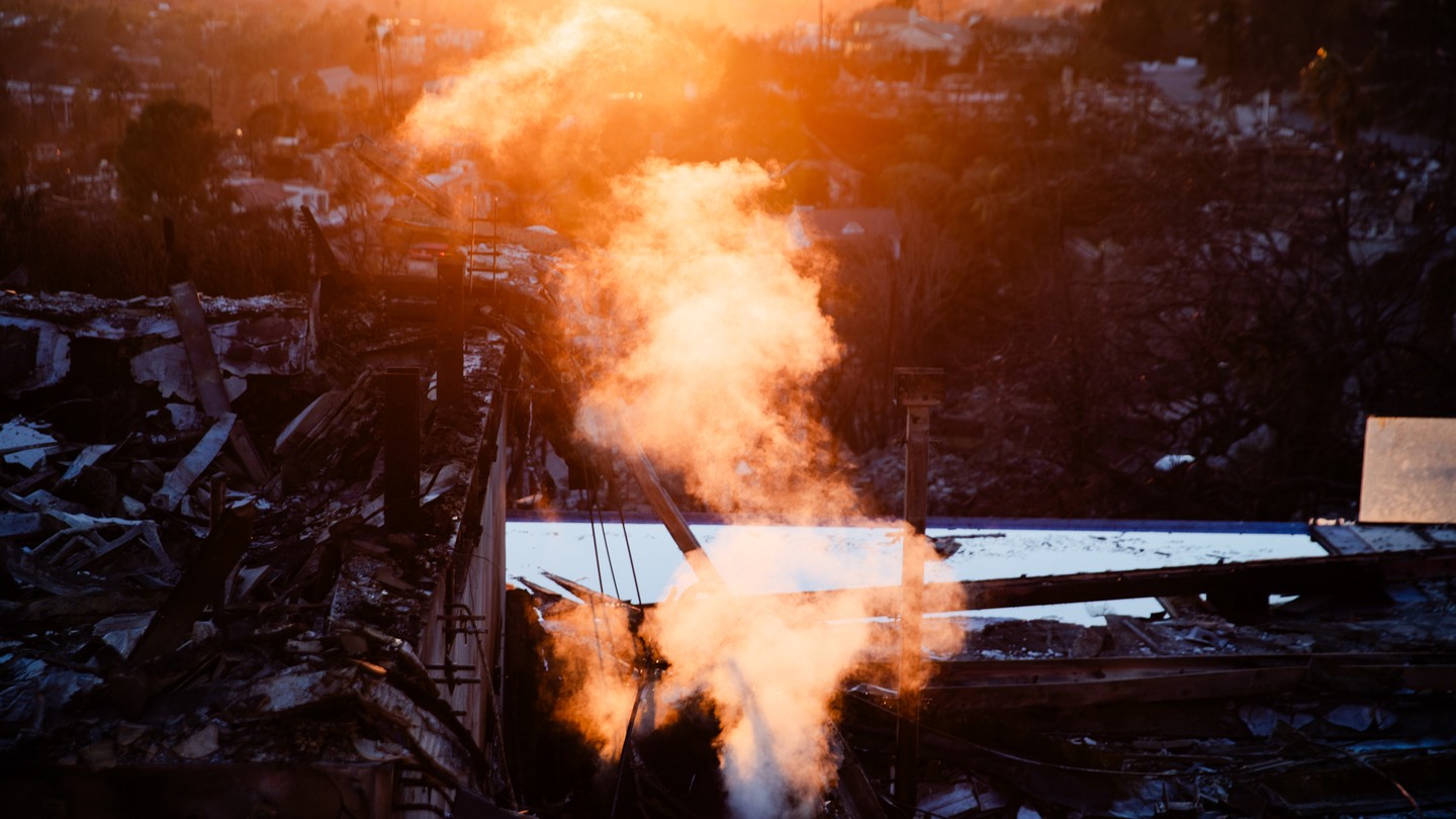 A color photograph of smoke rising in orange light above burned homes.