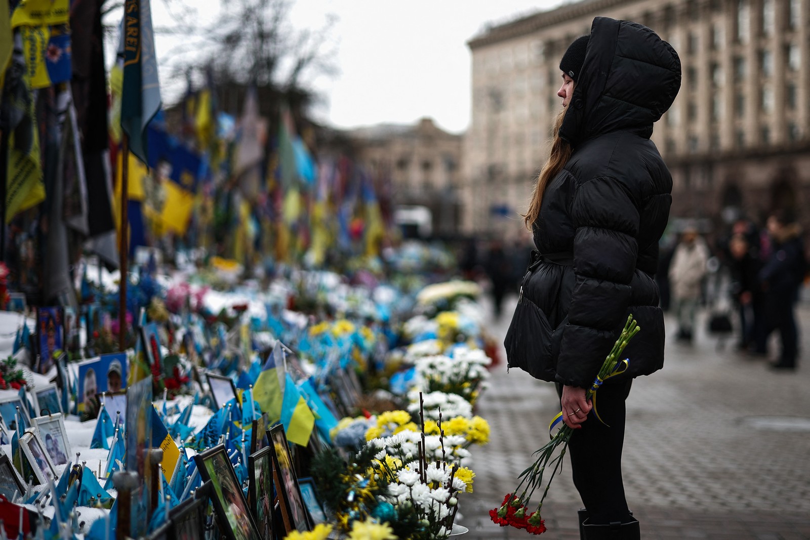 A person holds flowers, standing before a makeshift memorial for Ukrainian and foreign soldiers.