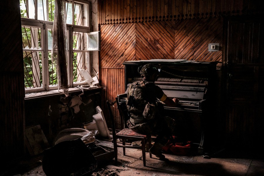 A soldier plays a piano inside a room in a damaged building.