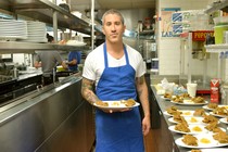Michael Solomonov holds a plate of food next to a row of plates of food on a restaurant kitchen counter.