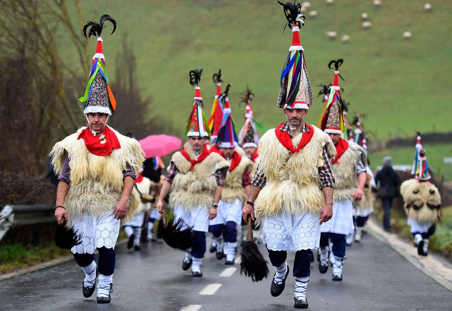 About a dozen men march in a rural road wearing traditional costumes.